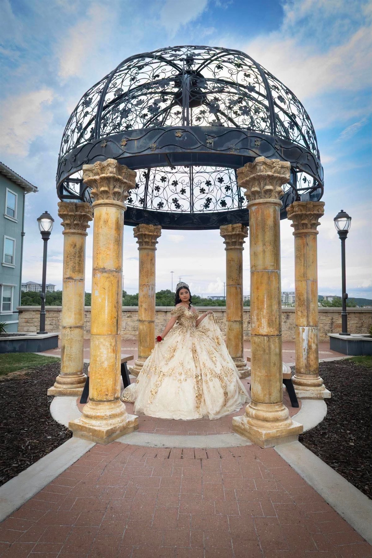 Quinceañera in a gold gown under a gazebo